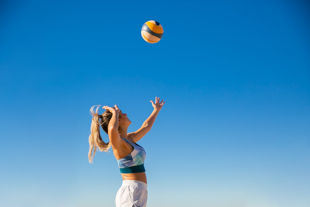 A woman spiking a volleyball on the beach under a clear blue sky, showcasing athletic skill and summer fun.